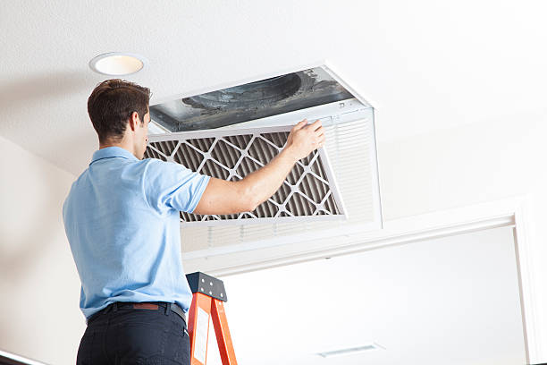 HVAC technician replacing a ceiling air filter on a ladder